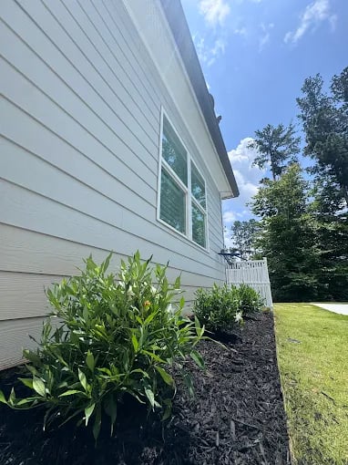 Well-maintained lawn and garden with fresh mulch beside white house